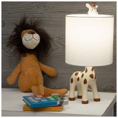 a stuffed giraffe sitting next to a lamp and books on a white table