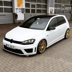 a white car with gold rims parked in front of a garage door on a brick road