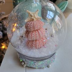 a snow globe with sea shells and starfish in it sitting on a table next to a christmas tree