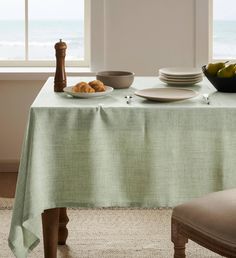 a table with plates and bowls on it in front of a window overlooking the ocean