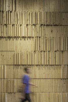 a blurry photo of a man walking past a wall made out of wooden planks