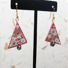 a pair of pink and green earrings on a black stand