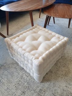 a white ottoman sitting on top of a carpeted floor next to a wooden table