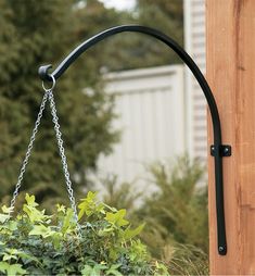 a bird feeder hanging from the side of a wooden pole next to bushes and trees