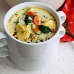 a white bowl filled with pasta and vegetables on top of a table next to a pot