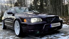 a purple car parked in the snow next to some trees and bushes with white rims