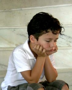 a young boy sitting on the ground with his hands to his face