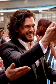 a man in a suit and tie holding his hand up to the camera with other people clapping behind him