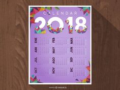 a purple calendar with colorful geometric shapes on the front and back cover is placed against a wooden background