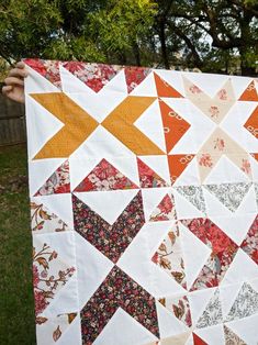 a person holding up a quilt made with different colors and shapes on it's sides