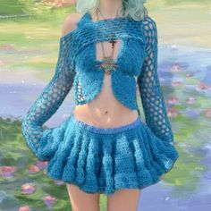 a doll is wearing a blue crochet outfit and posing in front of water