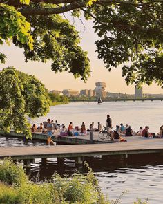 many people are sitting on the dock by the water and one person is riding a bike