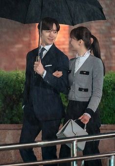 a man and woman standing under an umbrella in the rain, smiling at each other