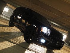 a black jeep parked in a parking garage with its lights on and the hood up