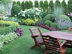 a wooden table sitting in the middle of a lush green field next to flowers and bushes