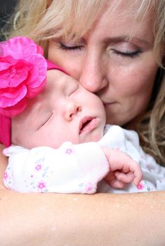 a woman holding a baby with a pink flower on it's head and kissing her face