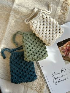 three crocheted bags sitting on top of a bed next to an open book