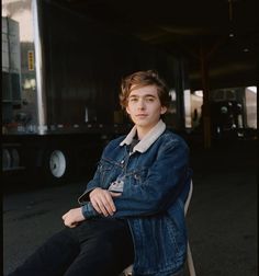 a young man is sitting on a chair in front of a semi - truck and looking at the camera