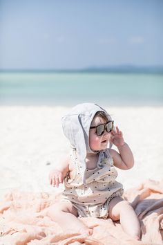 a baby sitting on the beach wearing sunglasses and a hood over it's head