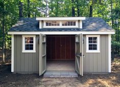 a small shed in the middle of a wooded area with doors open and windows on each side