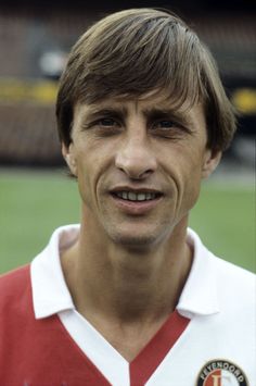 a man in a red and white shirt is smiling at the camera while standing on a soccer field