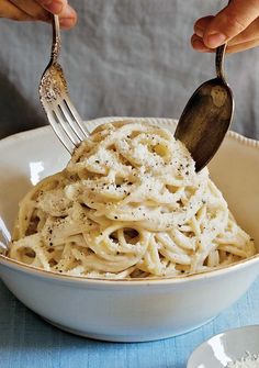 a person holding a fork and spoon over a bowl of pasta