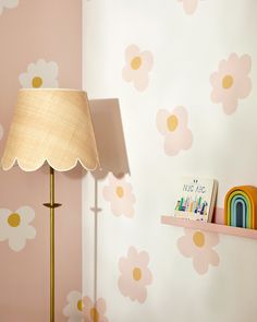 a lamp on a table next to a book shelf and flower wallpaper in a child's room