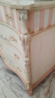 a pink and white striped chest with writing on the front, sitting on a marble floor