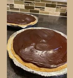 two pies with chocolate frosting sitting on top of a counter next to each other