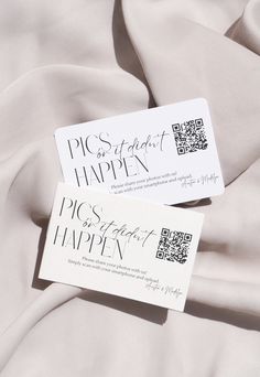 two white business cards sitting on top of a bed covered in sheets and satin material