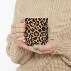 a woman holding a leopard print coffee mug in her right hand while wearing a beige sweater