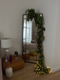 a mirror sitting on top of a wooden floor next to a christmas tree covered in lights