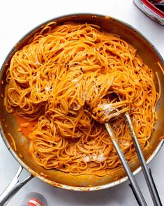 a pan filled with spaghetti and sauce on top of a white table next to cans of soda