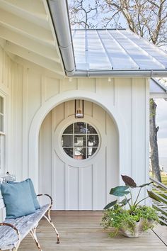 a white house with a door and window on the front porch, surrounded by potted plants