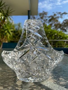 a clear glass vase sitting on top of a table next to some trees and bushes