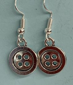 pair of earrings with silver and black buttons on them, hanging from hooks against a blue wall