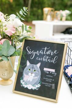 a sign that says signature cocktail sits on a table next to some flowers and plants