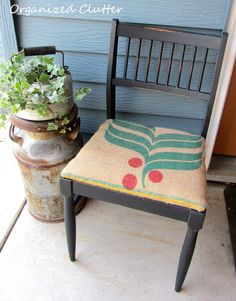 a chair with a cushion on it sitting next to a potted plant and an old metal trash can