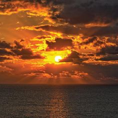 the sun is setting over the ocean with clouds