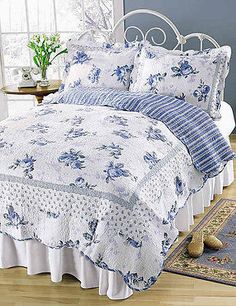 a bed with blue and white bedspread in a room next to a window