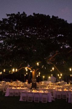 an outdoor dinner setup under a tree at night with lights on the branches and tables