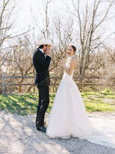 a bride and groom standing in front of a wooden fence, laughing at each other