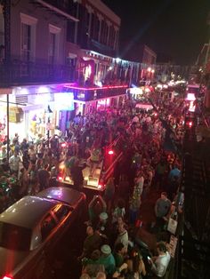 a crowded city street at night with lots of people on the sidewalk and cars parked in front of buildings