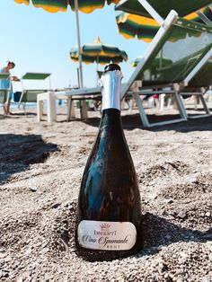 a bottle of wine sitting on top of a sandy beach next to chairs and umbrellas