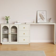 a white cabinet with glass doors and drawers in a room that has pink walls, hardwood floors and a rug on the floor