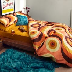 a bed with orange and yellow comforter in a bedroom next to a blue rug