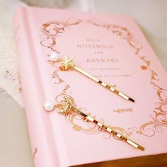 a pink notebook with two gold - tone hair pins on it