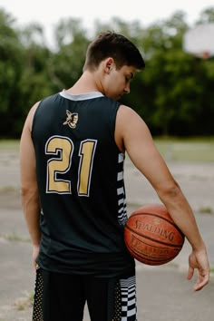 a young man holding a basketball on top of a basketball court with trees in the background