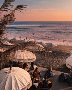 people sitting under umbrellas on the beach at sunset