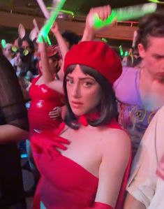 a group of people standing around each other at a party with one woman wearing a red dress